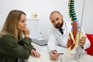 Médico explicando modelo da coluna vertebral para paciente jovem