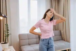 Mulher sentindo desconforto por causa de dor de cabeça e nas costas enquanto estava em sua sala de estar