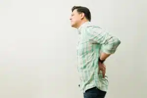 Homem fazendo caretas enquanto toca na parte inferior das costas.