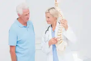 Médica explica ao paciente os riscos da hérnia de disco extrusa utilizando um modelo anatômico da coluna vertebral durante a consulta.