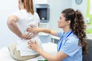 Médica avaliando a paciente para diagnosticar a síndrome facetária crônica, identificando a localização e as características das dores na região da coluna.